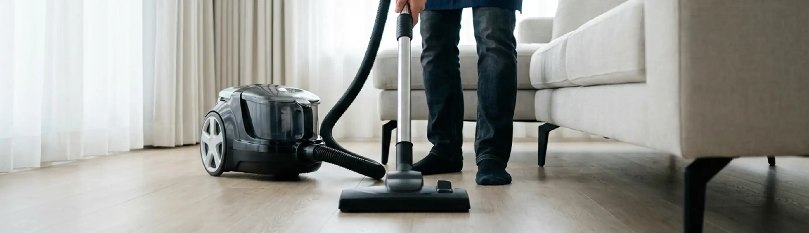 Professional house cleaner vacuuming a living room floor with a canister vacuum cleaner, Cleveland, OH.