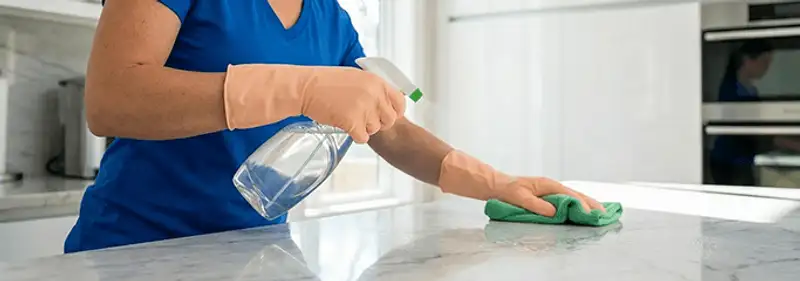 Maid service worker spraying and wiping a kitchen countertop with a microfiber cloth for sanitizing, Cleveland, OH.