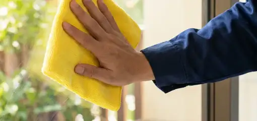 House cleaner wiping a glass window with a yellow microfiber cloth for streak-free cleaning, Cleveland, OH.